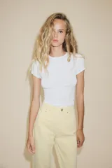 Jeans de mujer, tiro alto, color azul medio con efecto desgastado (lavado claro en muslos y oscuro en bordes). Corte recto y ancho (mom fit) con cinco bolsillos y cierre frontal de botón y cremallera.