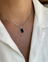 Collar con cadena de eslabones tipo caja plateada y un dije rectangular con borde plateado y centro de piedra negra pulida.