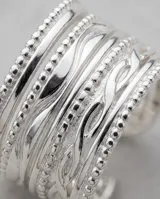 Anillo ancho de acero plateado con diseño texturizado de líneas múltiples y ajuste abierto.