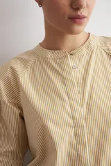 Camisa de manga corta color beige con sutiles rayas verticales blancas, cuello mao y cierre frontal oculto con botones.