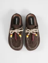 Mocasines tipo mule color marrón con textura de gamuza, costuras decorativas en el borde y cordones con cuentas de acrílico de colores.