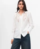 Camisa blanca de manga larga con detalles bordados calados en el frente y puños anchos.