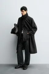 Trench de corte oversized confeccionado en tejido compacto con mezcla de lana. Presenta cuello solapa, cierre frontal con botonadura, mangas largas y bolsillos de vivo en la cadera.
