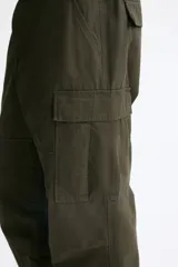 Pantalón cargo de lona de algodón con bolsillos laterales tipo cargo, bolsillos traseros con solapa y pliegues en las rodillas. Presenta cierre con botón y ajuste en la cintura.