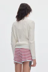 Cardigan de punto color marfil con cierre frontal completo, cuello alto y detalles de rayas en contraste en cuello, puños y ruedo. Presenta diseño de ochos verticales.