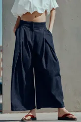 Pantalón tipo culotte de tiro alto confeccionado en denim azul oscuro. Presenta pinzas delanteras, pernera ancha y corta, bolsillos laterales ocultos y cierre frontal con cremallera, botón y ganchos.