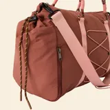 Bolso de deporte color marrón con detalles en rosa claro. Presenta correas de mano tipo cuerda, una correa ajustable para el hombro, un sistema de cordones elásticos decorativos en el frente y bolsillos laterales con cierre.