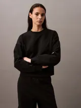 Buzo Calvin Klein de felpa francesa color negro, de corte holgado y diseño con cuello redondo. Cuenta con mangas largas, puños y dobladillo acanalados, y lleva el logo retro de la marca bordado discretamente en el pecho.