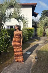 Vestido largo strapless, ajustado al cuerpo, con estampado batik en tonos marrones y naranjas.