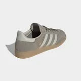Championes Adidas Handball Spezial de diseño clásico, confeccionados en ante vacuno suave color gris con las icónicas tres tiras laterales en tono más claro. Presentan suela de goma color caramelo y cierre de cordones.