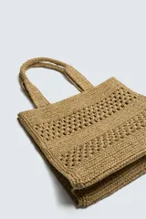 Bolso tipo shopper de diseño trenzado en color tostado, con estructura rectangular, dos asas de mano y compartimento principal abierto.