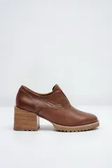 Zapato de cuero color beige, con taco de madera y suela dentada. Presenta un diseño slip-on con detalles de textura en relieve en los laterales y el empeine.