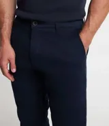 Pantalón de vestir para hombre, color beige claro, de corte slim y sastrería. Presenta cierre frontal con botón y cremallera, y bolsillos laterales y traseros.