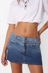 Minifalda de jean azul con lavado degradé, tiro medio con doble cintura, bolsillos delanteros y traseros, cierre metálico y dos botones personalizados.