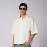 Camisa de manga corta color marfil, confeccionada en 100% algodón con calce boxy, cuello camisero, cierre frontal de botones y diseño con bordado sutil en la parte inferior.