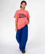 Remera color crudo con cuello redondo y manga corta. Estampado frontal de una banderín marrón con la palabra "BOSTON" en letras doradas con efecto glitter. Incluye dos pines decorativos prendidos en la zona superior derecha del pecho.