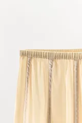 Pantalón de tiro medio confeccionado en algodón, con cintura elástica y diseño de corte recto. Presenta aplicaciones verticales de cintas o lazadas a lo largo de las piernas.