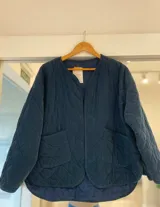 Casaca de pana acolchada en color azul oscuro, con diseño de cuello redondo, sin cierre frontal y dos bolsillos delanteros aplicados. Presenta un patrón de costuras en forma de rombos.