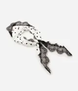 Pañuelo triangular de poliéster con acabado satinado, color blanco con estampado de lunares negros y detalle de encaje negro aplicado en uno de sus bordes.