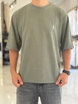 Remera oversize de tejido texturizado en color verde militar, con cuello redondo y mangas cortas. Presenta un pequeño bordado blanco en el pecho.