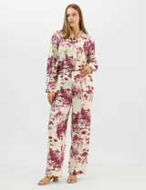 Conjunto de dos piezas compuesto por camisa de manga larga con cuello solapa y botones frontales, y pantalón de tiro alto con pierna recta y bolsillos laterales. Ambas prendas presentan un estampado paisajístico en tonos marrones sobre fondo crema.