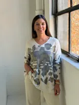 Sweater de punto con cuello en V y mangas largas, de diseño holgado. Presenta un estampado abstracto en tonos verdes con detalles metalizados en color dorado sobre una base de color crema.