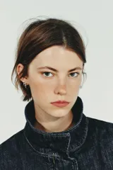 Cazadora de denim azul oscuro con cuello solapa, cierre frontal con cremallera y botones a presión ocultos. Presenta mangas largas tipo murciélago con puños, bolsillos de vivo en el delantero y bajo elástico ajustable con cordones.