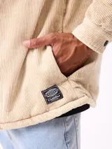 Sobrecamisa de pana color beige, con cierre frontal de botones a presión, dos bolsillos frontales con solapa y bolsillos laterales. Presenta cuello clásico y diseño acolchado con forro interior.