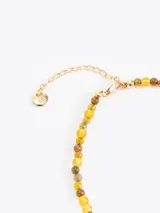 Collar de mostacillas de vidrio en tonos verdes y negros, con dije metálico en forma de mariquita azul oscuro con detalles plateados. Incluye cadena regulable de acero inoxidable.