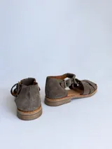 Sandalias cangrejeras de gamuza color marrón, con punta redonda, taco bajo, talonera cerrada y tira con hebilla metálica ajustable en el tobillo.