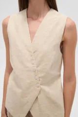 Chaleco color beige claro, sin mangas, con escote en V profundo y cierre frontal asimétrico con botones.