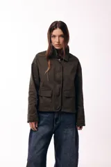 Campera corta de color verde militar, con cuello alto estructurado, cierre frontal oculto y dos bolsillos delanteros con solapa. Presenta un corte recto y minimalista.