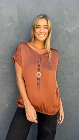 Blusa de satén color terracota con cuello en V, mangas cortas con dobladillo y ruedo elástico. Presenta un diseño fluido y elegante.