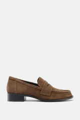 Mocasín de mujer confeccionado en serraje color marrón, con detalle de antifaz en el empeine, costuras a la vista y punta redonda. Cuenta con un pequeño tacón cuadrado.