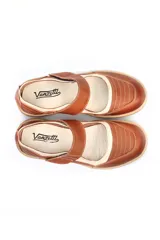 Zapato tipo guillermina de cuero, con diseño combinado en tonos marrón y beige. Presenta cierre con tira de velcro en el empeine, costuras decorativas visibles y suela plana de goma en color tostado.