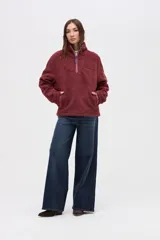 Buzo de sherpa con textura capitoneada, color bordó, con cuello alto y cierre frontal parcial. Presenta bolsillos laterales y calce relajado.