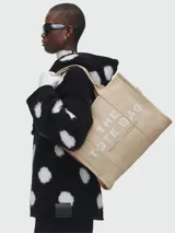 Bolso tipo tote de gran tamaño en color beige, confeccionado en lona resistente. Presenta el logo distintivo de la marca estampado en la parte frontal con letras blancas. Cuenta con doble asa superior para llevar al hombro y cierre superior con cremallera.