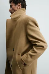 Abrigo largo color camel, de corte relajado (relaxed fit), confeccionado en tejido con mezcla de lana. Presenta cuello con solapas de muesca, manga larga, bolsillos de vivo en cadera, bolsillo interior y cierre frontal de botonadura cruzada.
