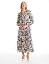 Vestido maxi de satén con estampado floral en tonos negro y beige. Presenta escote en V, hombros fruncidos, mangas largas con puños elásticos y cintura con detalle de punto smock. La falda tiene un diseño escalonado con vuelo.