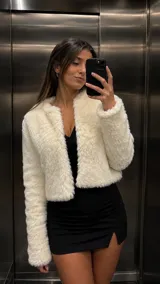 Chaqueta de piel sintética blanca con textura de peluche, cuello redondo y diseño corto sin botones.