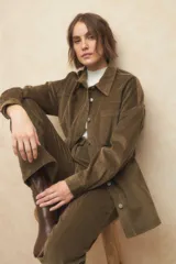 Sobrecamisa de pana color verde oliva, con cuello camisero, cierre frontal con botones metálicos, manga larga y bolsillo frontal. Incluye un lazo ajustable en la cintura.