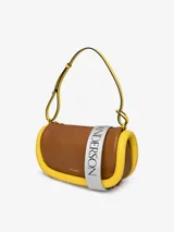 Bolso de hombro JW Anderson modelo Bumper-15, color rosa con ribetes tubulares acolchados en verde oscuro. Tiene correa de hombro ajustable, cierre con cremallera superior y logo estampado en el frente.