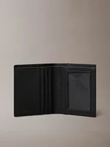 Billetera plegada Calvin Klein de cuero con textura granulada. Cuenta con compartimento para billetes, cinco ranuras para tarjetas y una solapa transparente para identificación. Presenta el logo de la marca grabado en lámina metálica en el frente.