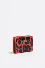 Billetera pequeña de estructura rígida con acabado brillante y estampado animal print en tonos rojos y negros. Presenta cierre de cremallera perimetral, logo metálico dorado en el frente y tarjetero interior.