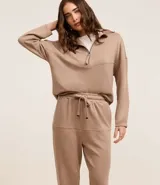 Conjunto de dos piezas color beige, compuesto por un sweater de manga larga con cuello polo y cierre frontal parcial, y un pantalón jogger a juego con cordón ajustable en la cintura.