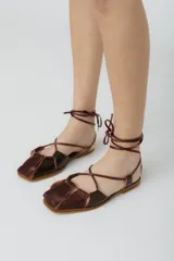 Sandalias bajas de cuero color marrón con tiras que se atan al tobillo.