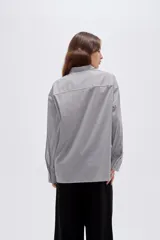 Camisa de algodón a rayas grises y blancas, de corte holgado, con cuello camisero, manga larga y cierre frontal de botones.