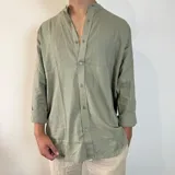 Camisa de manga larga en tejido de lino, color blanco, con cuello mao y cierre frontal de botones. Presenta un corte oversize y mangas con puños doblados.