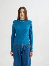 Polera de manga larga confeccionada en tela rib color bordó, con cuello alto y hombreras. Presenta costuras a la vista con pespuntes en hilo de color contrastante en el cuello, puños, hombros y ruedo.