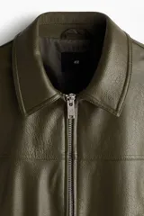Cazadora estilo bomber en tejido revestido color verde militar, con cuello clásico, cierre frontal de cremallera metálica, bolsillos laterales y elástico fruncido en el bajo y los puños.